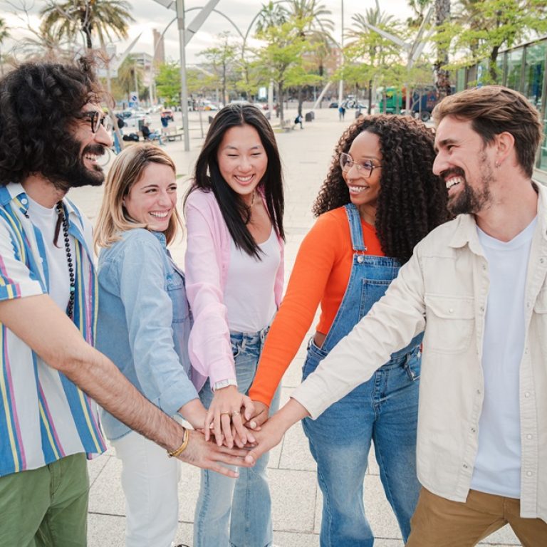 Meeting of smiling young adult people, men and women stacking hands showing unity or support enjoying together outside. Group of cheerful best friends community having fun cooperating together. Team. High quality photo
